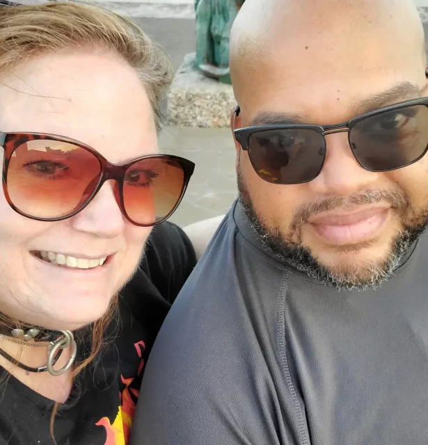 An image of Invictuz and BebeBlueEyes on the day of Bebe's collaring. She is wearing her Leather collar with a silver ring and they are both smiling at the camera